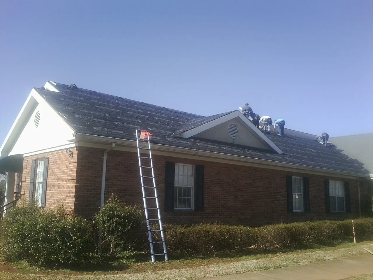 Crew tearing shingles off a brick ranch roof with a ladder set — Emergency Roof Repair work by our crew in Spencer